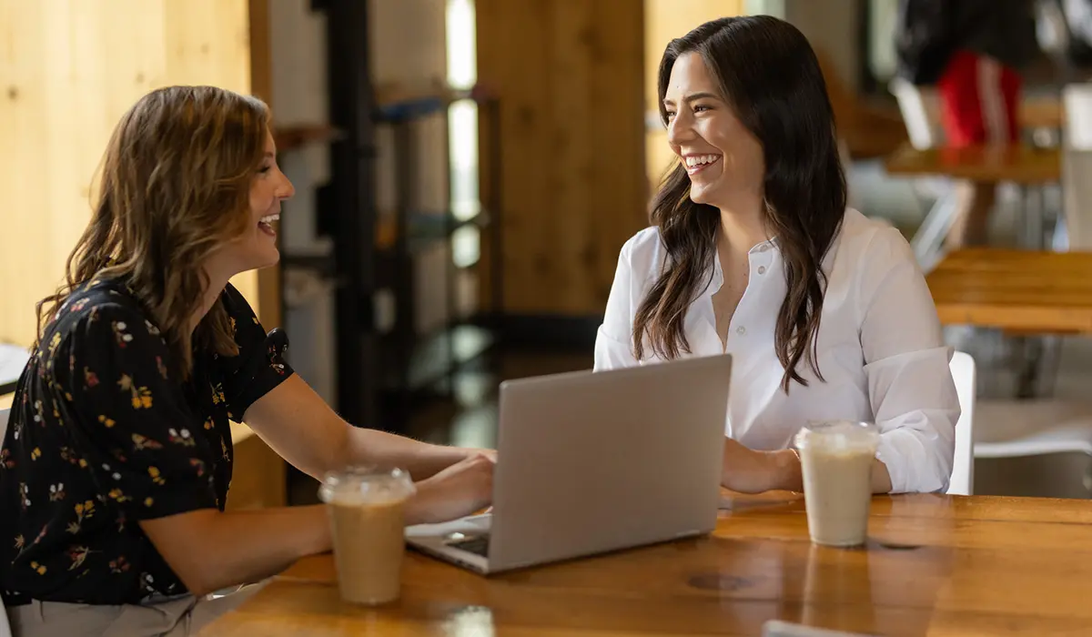 Two professionals collaborating in a modern office setting with coffee and a laptop, showcasing workplace design and collaboration.